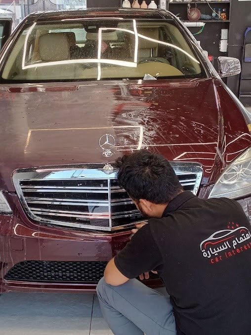 أحد أفراد فريق اهتمام السيارة يعمل على مقدمة سيارة حمراء
